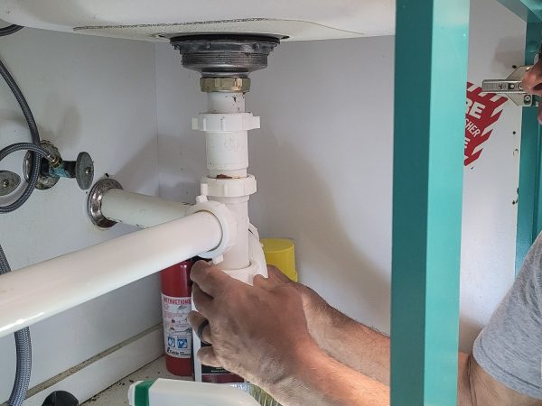 Professional Plumber working on kitchen utilities under sink stopping a water leak in repairs.
